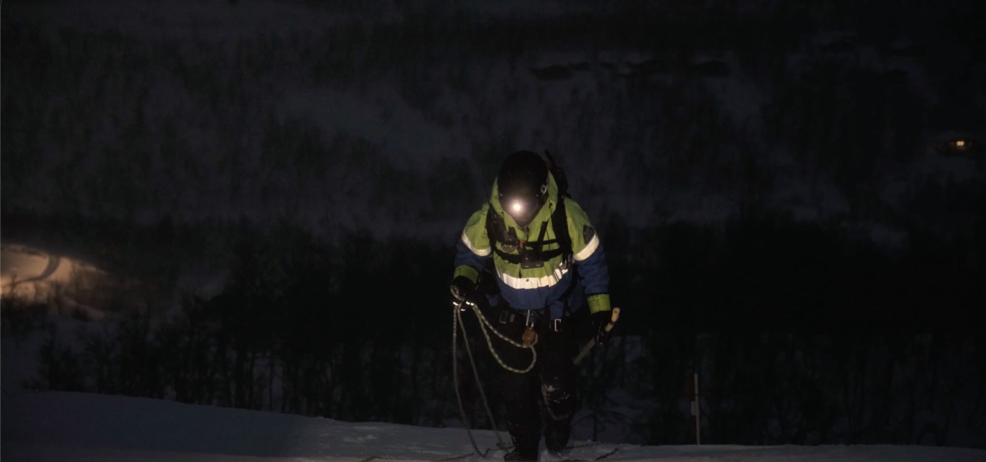 Lavinsprängare med rep går uppför fjället i mörkret